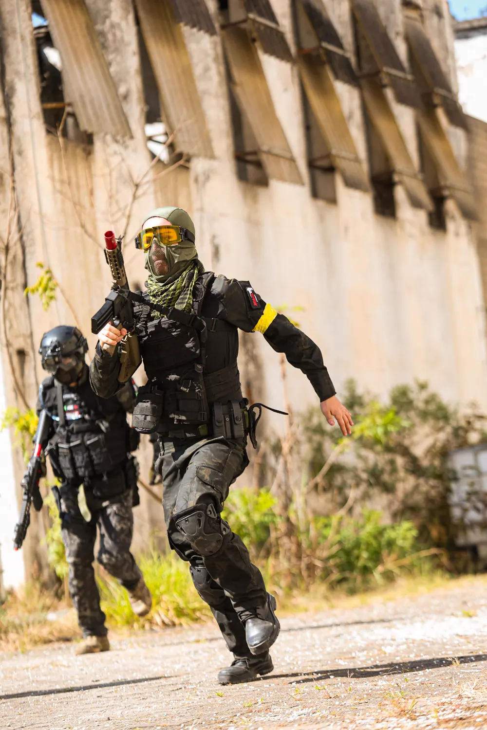 Dupla avança em corrida junto ao galpão; o jogador da frente, de máscara e óculos amarelos, sinaliza para o time.