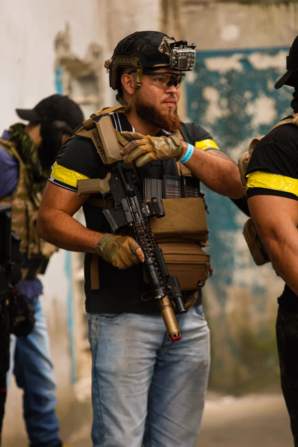 Operador ruivo de camiseta e jeans, com colete e fita amarela no braço, observa o campo antes da partida.